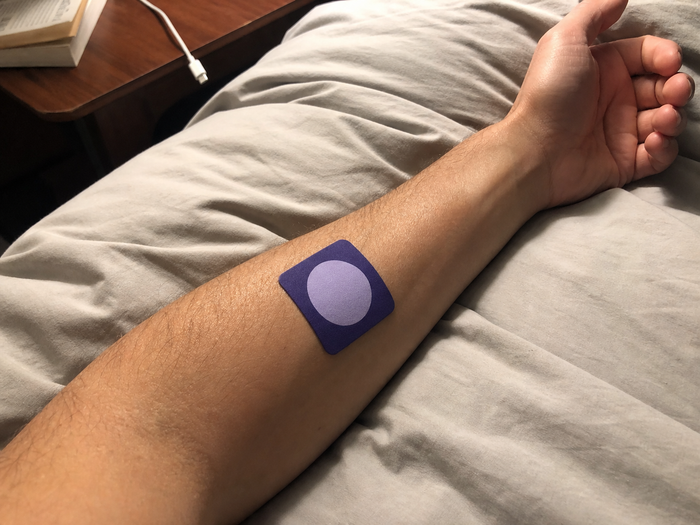 Close-up of a Pure Patch Sleep Patch on a forearm resting on gray bedding.